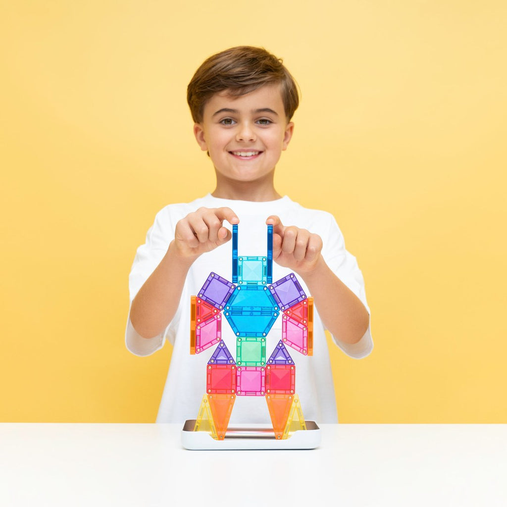 Smiling girl holding a mini magnetic tile rocket beside her sticker-covered CONNETIX travel tin