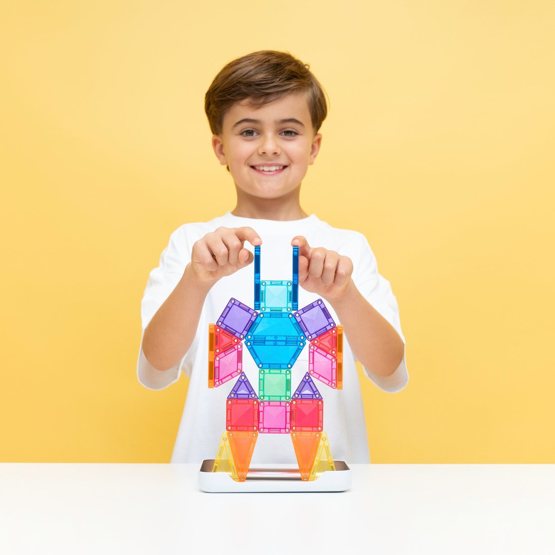 Smiling girl holding a mini magnetic tile rocket beside her sticker-covered CONNETIX travel tin