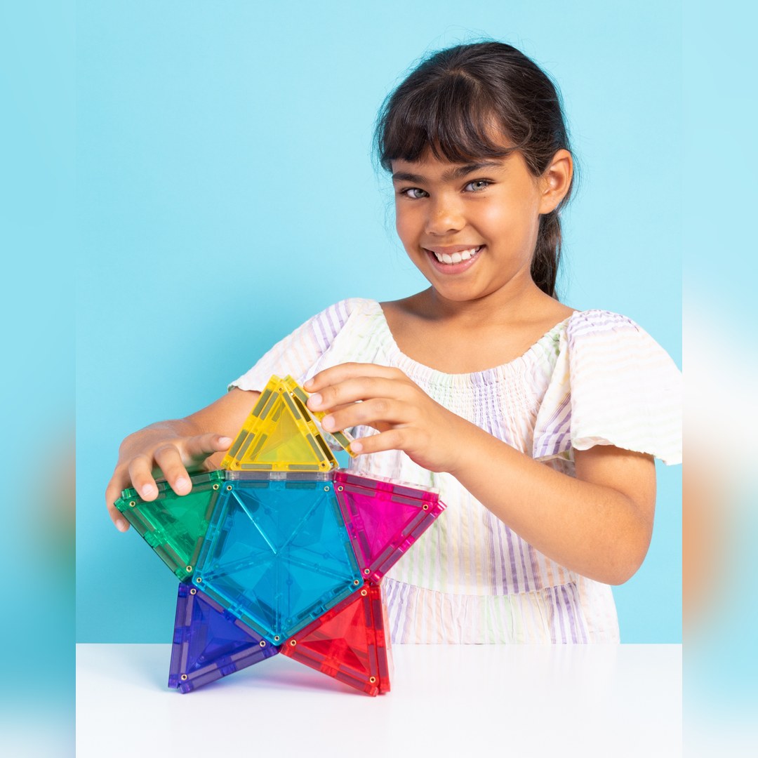 Smiling girl building a rainbow star from CONNETIX pentagon and triangle magnetic tiles
