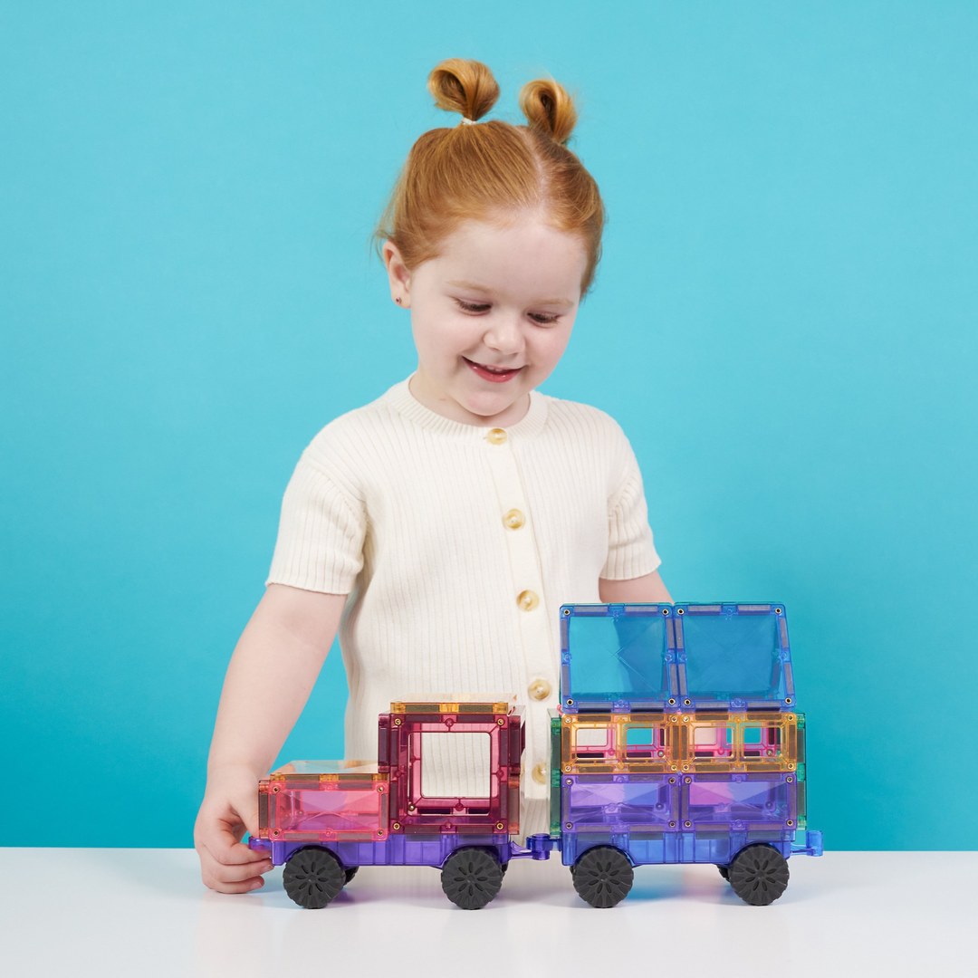 Smiling girl pushing a pastel truck and trailer built from CONNETIX magnetic tiles