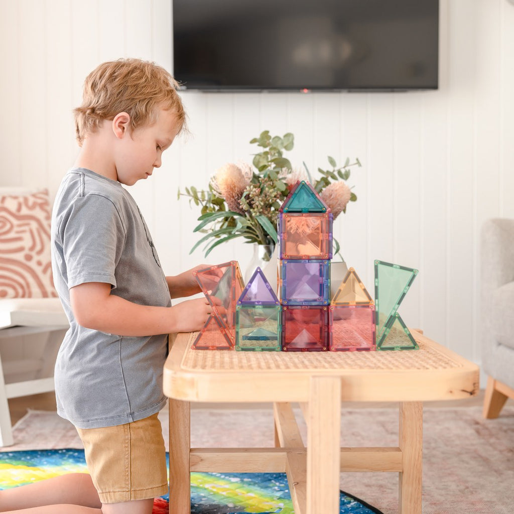 Boy building a pastel CONNETIX magnetic tile tower on a rattan coffee table