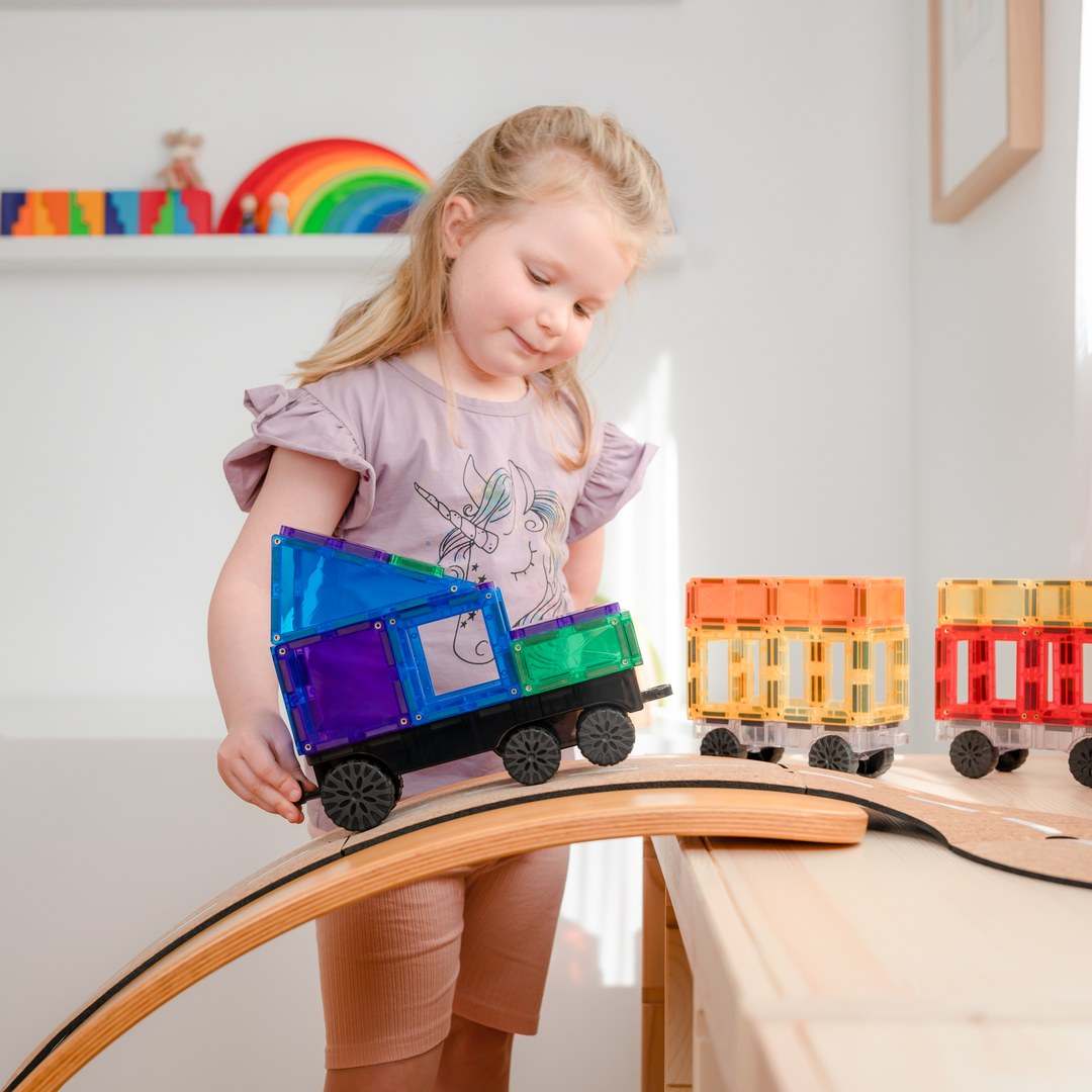 Smiling girl driving a CONNETIX magnetic tile truck over a wooden bridge
