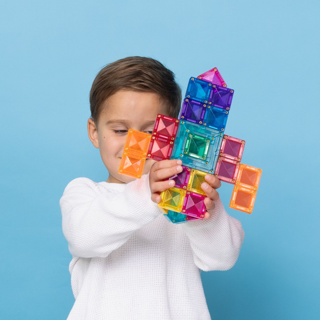 Boy holding up a rainbow rocket built from CONNETIX portal and square tiles