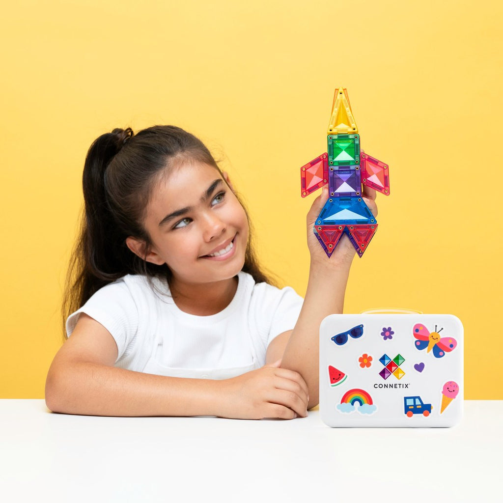 Girl holding up a CONNETIX mini tile decorated with a bee sticker beside a flower build