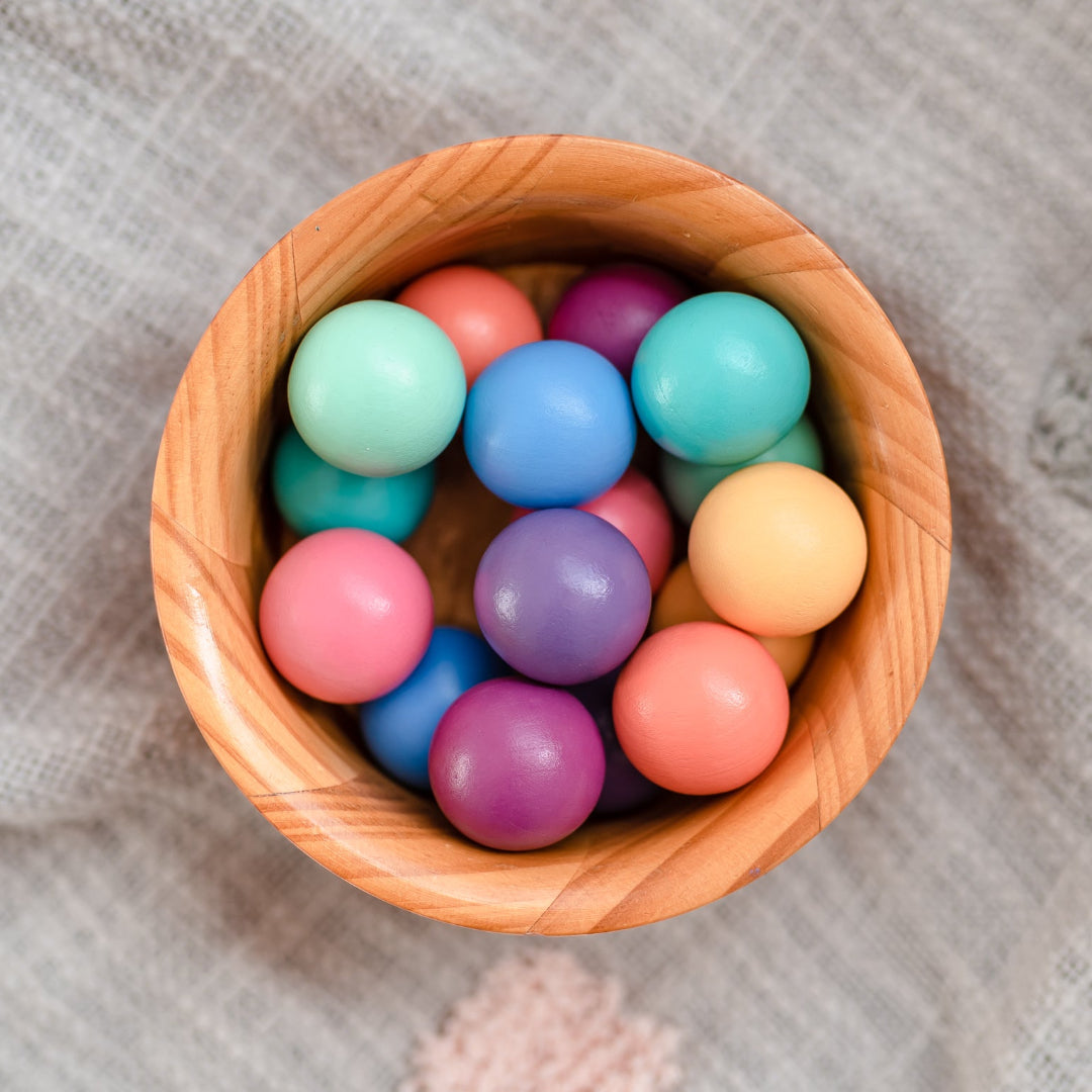 Eight pastel CONNETIX wooden ball run balls in a wooden bowl