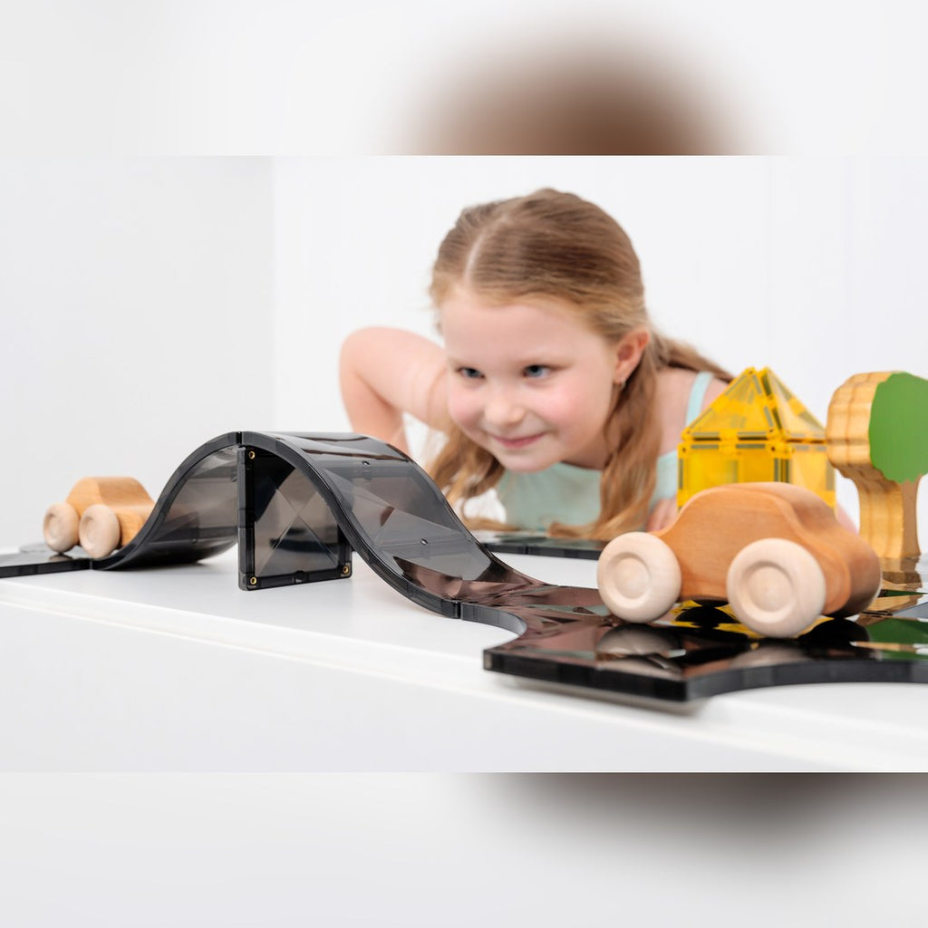 Smiling girl watching a wooden car on a curved CONNETIX magnetic tile ramp