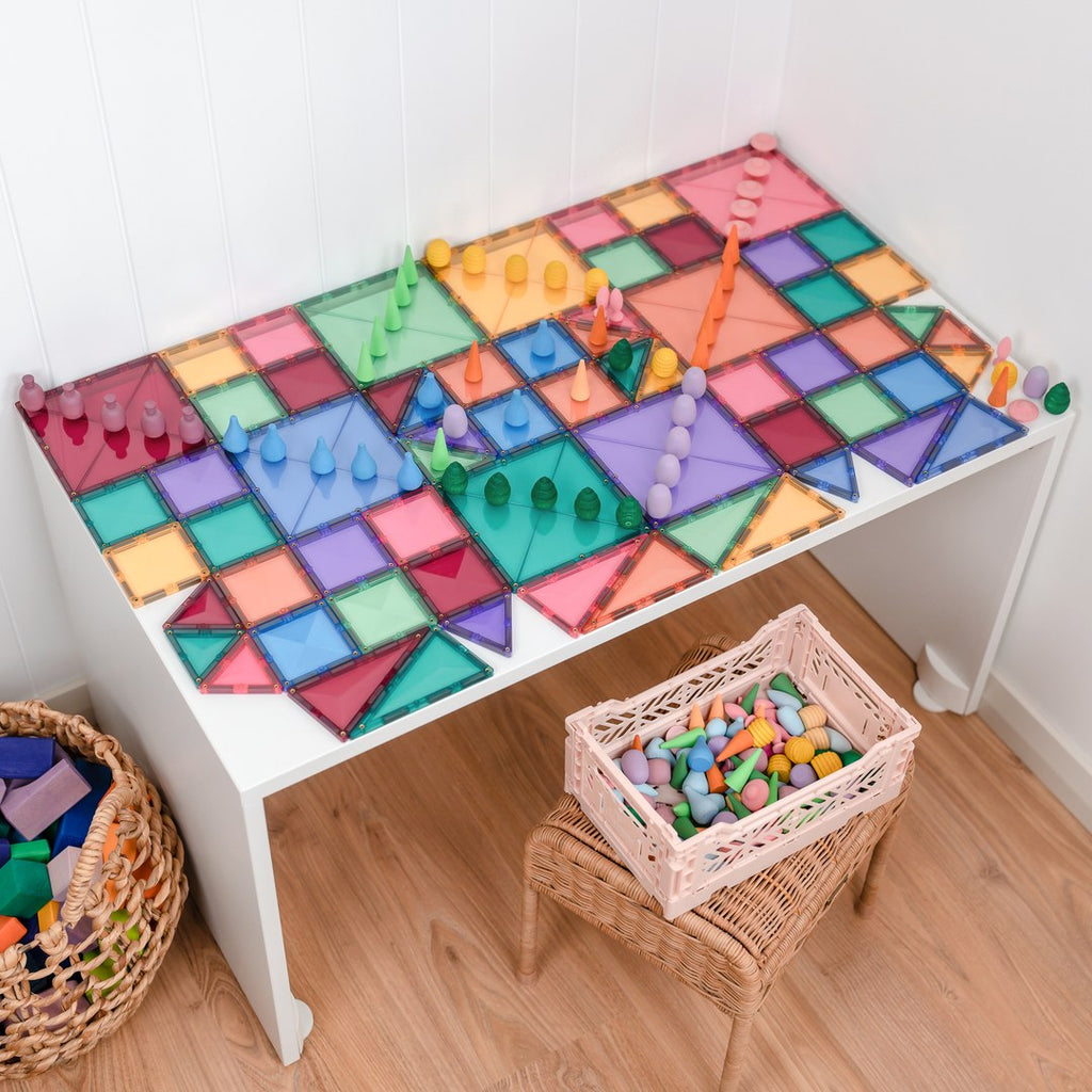 Pastel CONNETIX magnetic tiles laid flat as a play mat with wooden peg pieces on a table