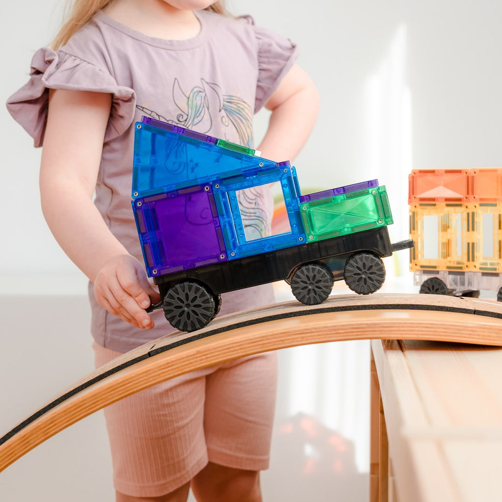 Child rolling a CONNETIX magnetic tile truck over a wooden arch