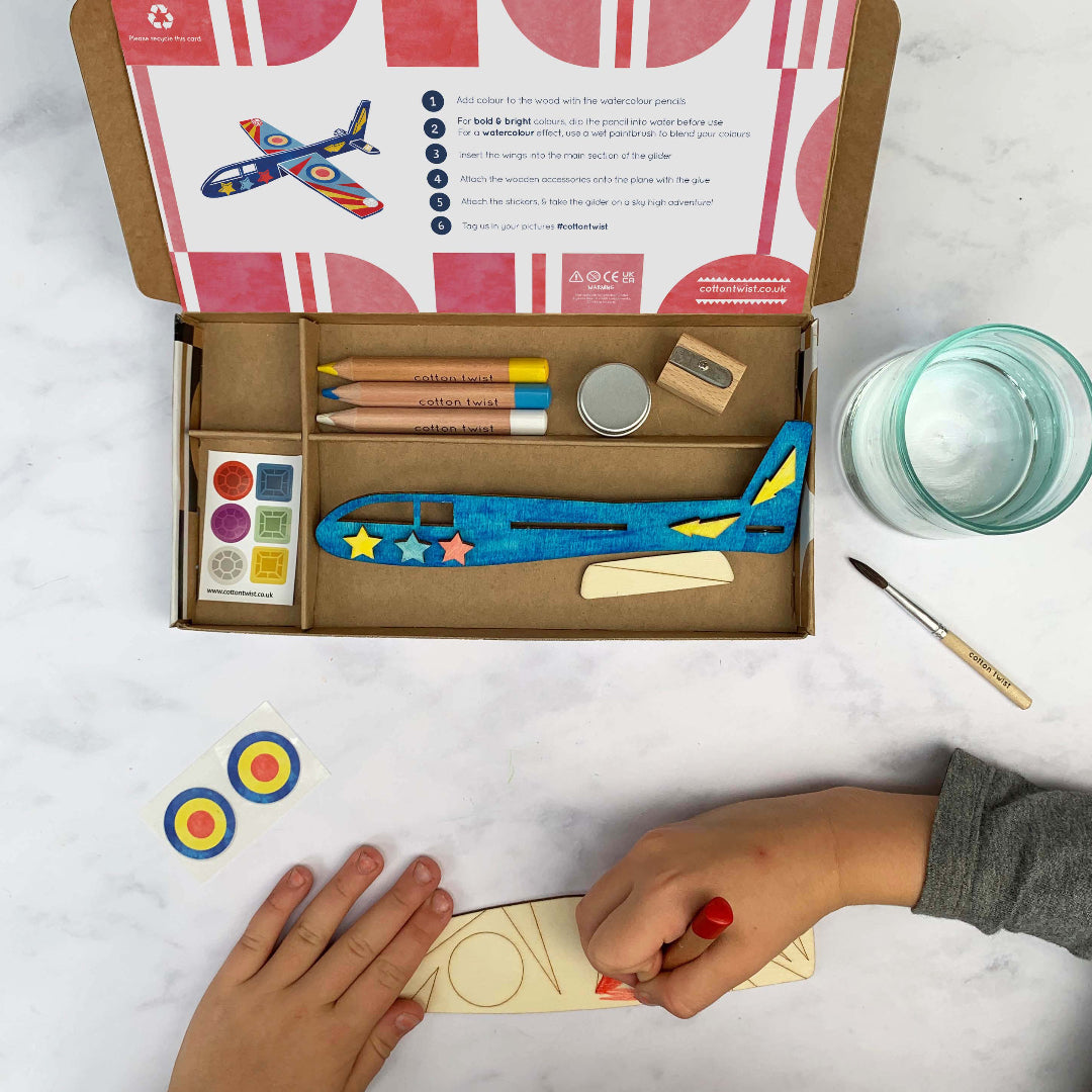 Children's craft kit with airplane model, markers, and paint on a white surface.