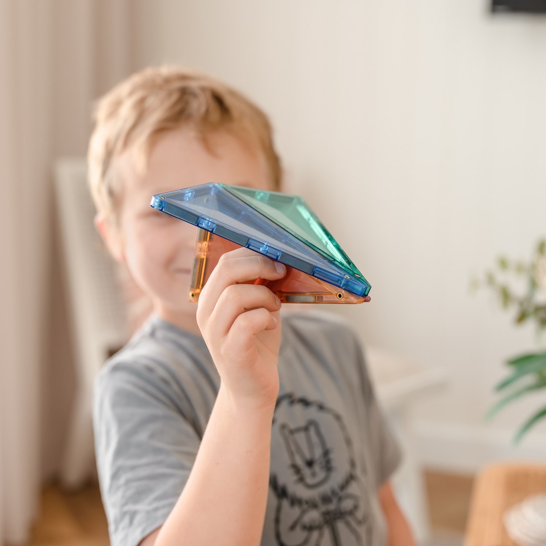 Smiling boy holding up a pastel CONNETIX triangle tile shape like a paper plane