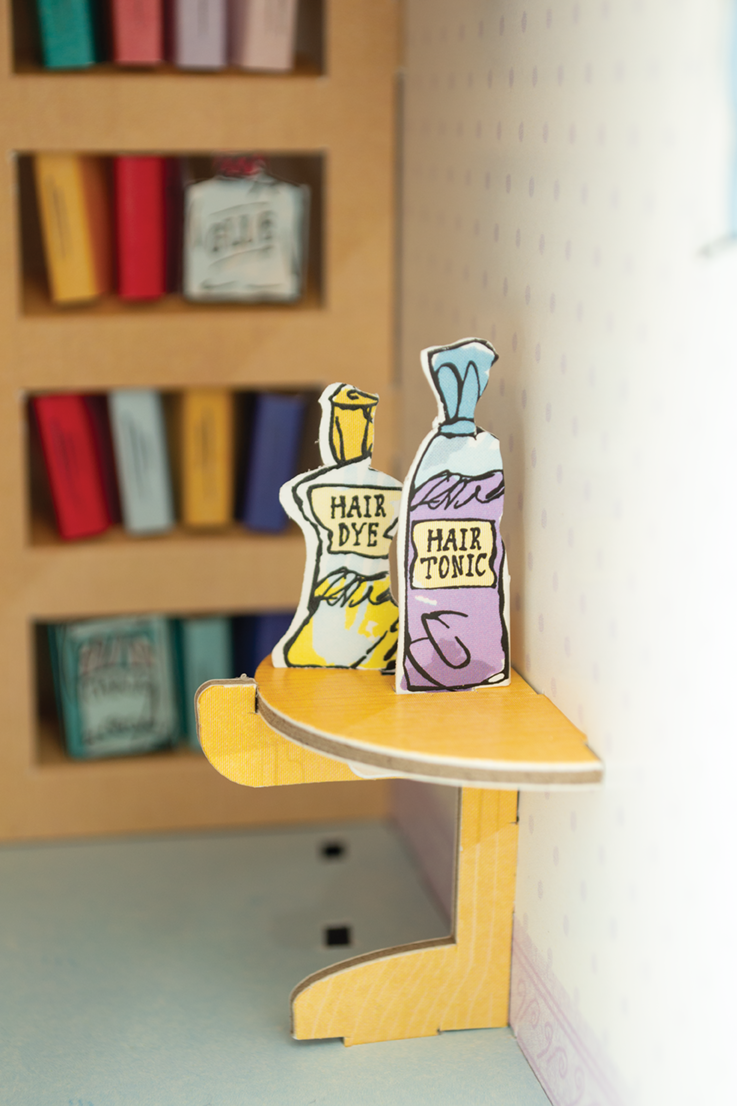 Model of hair dye and tonic bottles on a small table with a bookshelf in the background.