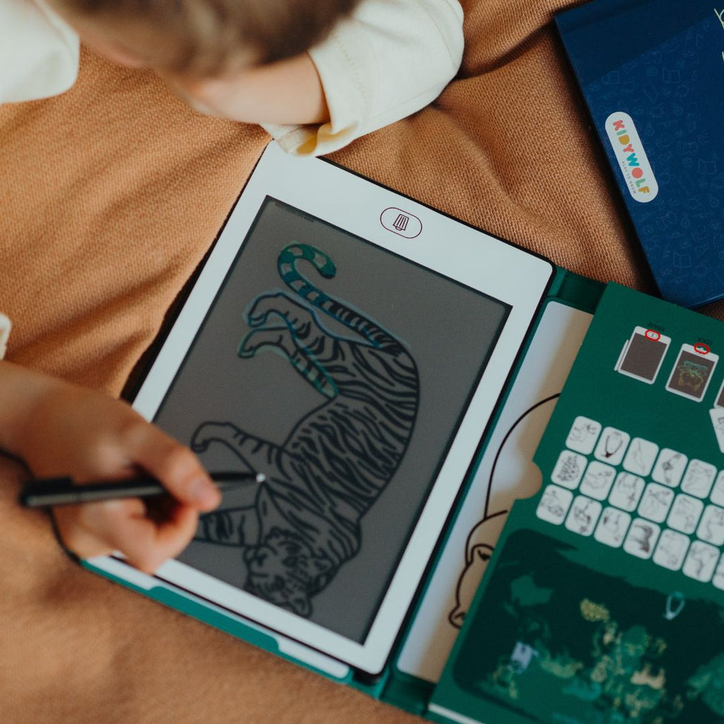 Overhead view of a child tracing a tiger on the KIDYDRAW MINI tablet with the stylus, green Animals card holder open beside it