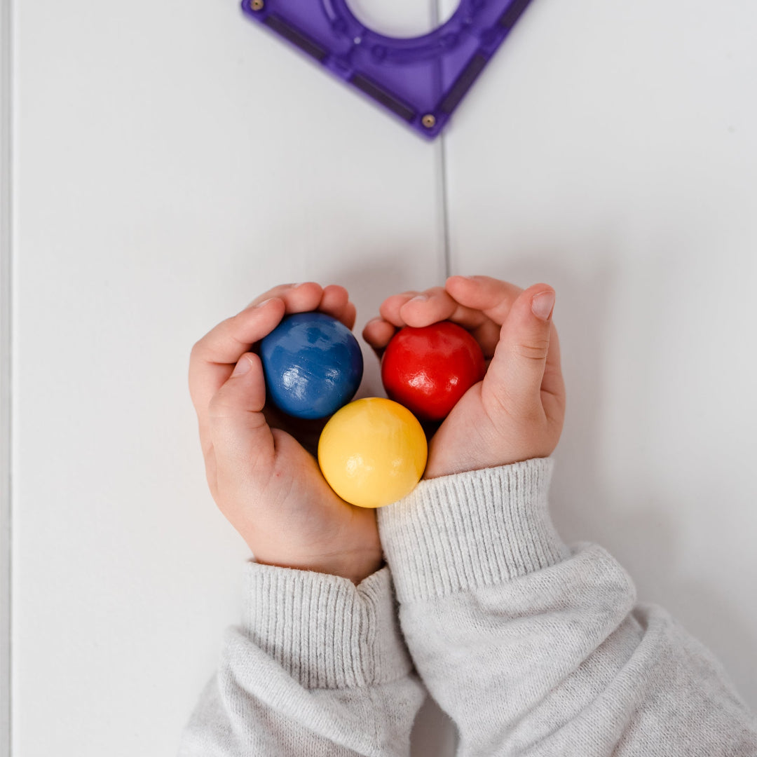 Child's hands holding three colourful CONNETIX wooden ball run balls