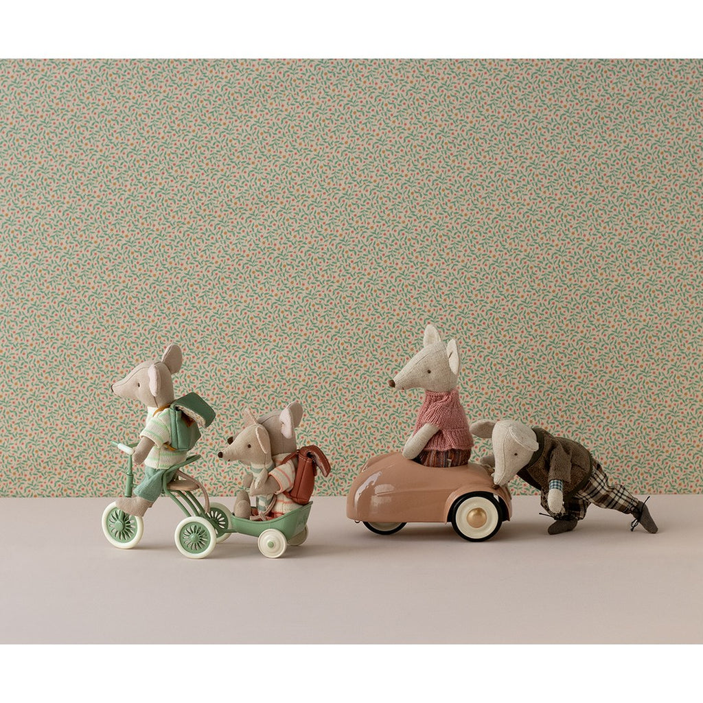 Maileg mice riding a green tricycle with trailer next to a pink mouse car on a floral wallpaper set