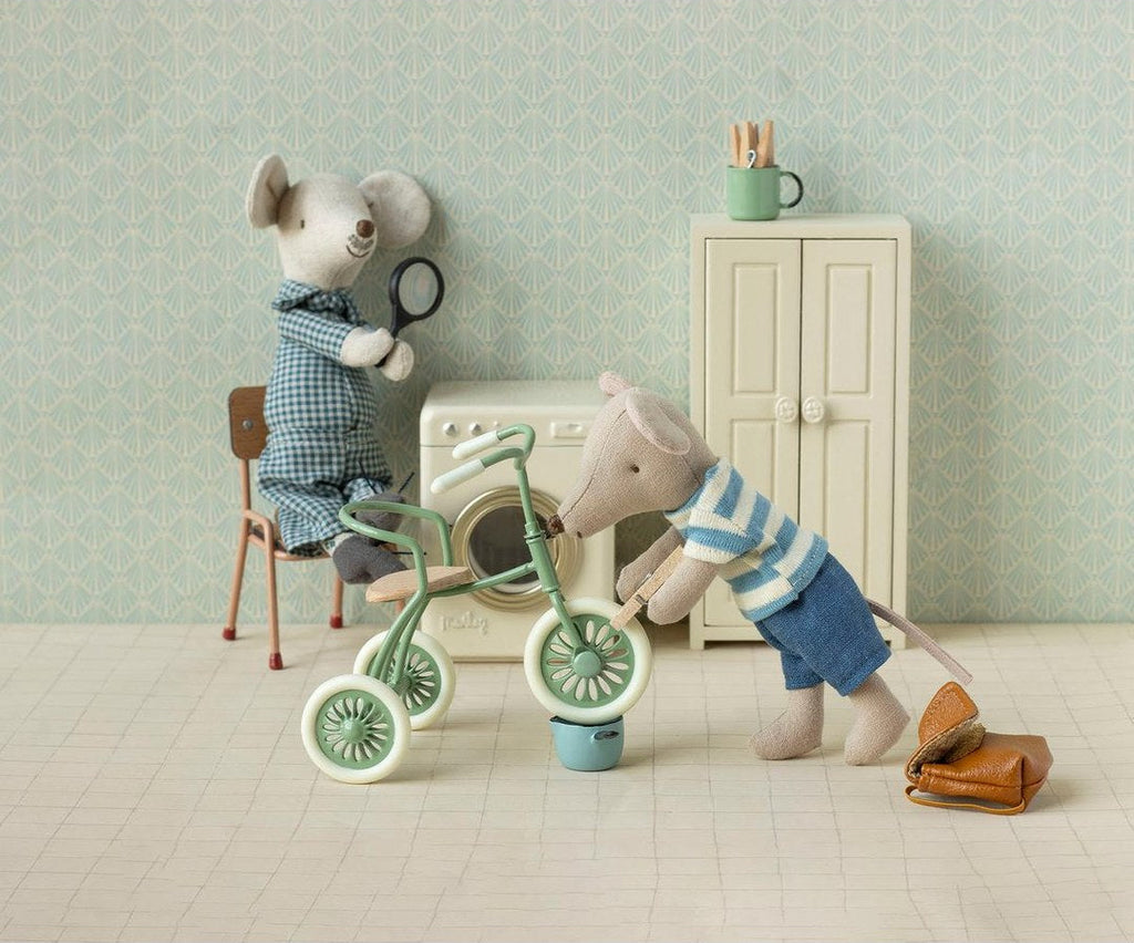 Maileg mice in a laundry room with a green tricycle, washing machine and cream wardrobe