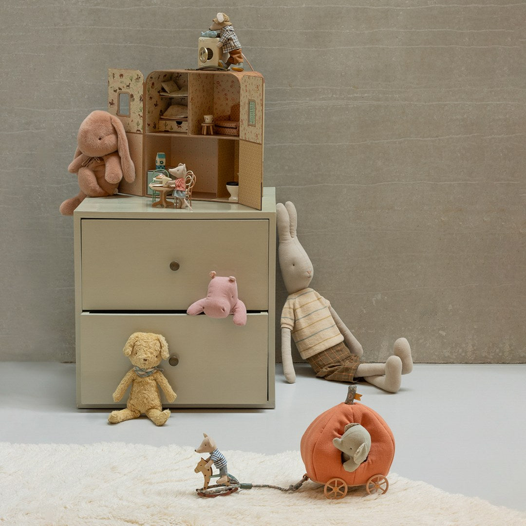 Maileg mouse riding a rocking horse pulling the orange pumpkin carriage with a mouse inside, beside a chest of drawers with plush animals