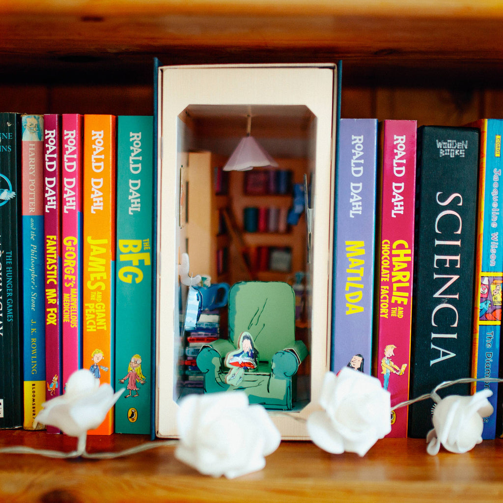 Bookshelf with books and a small model of a room inside one of the books.