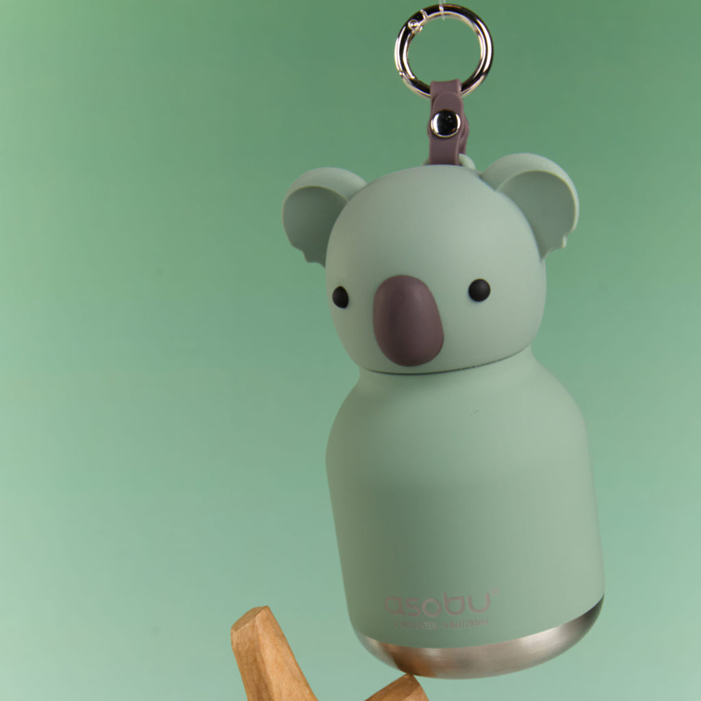 Mint green koala-shaped bottle with a bell on a wooden branch against a light green background