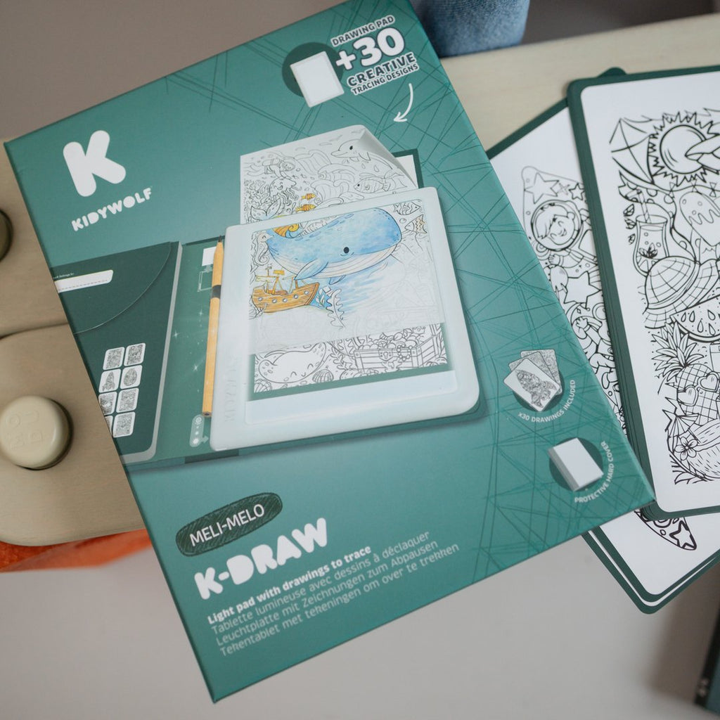 Close-up of the K-DRAW Meli Melo box beside illustration sheets