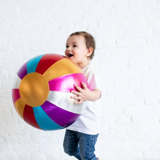 Child holding a colorful beach ball against a white brick wall