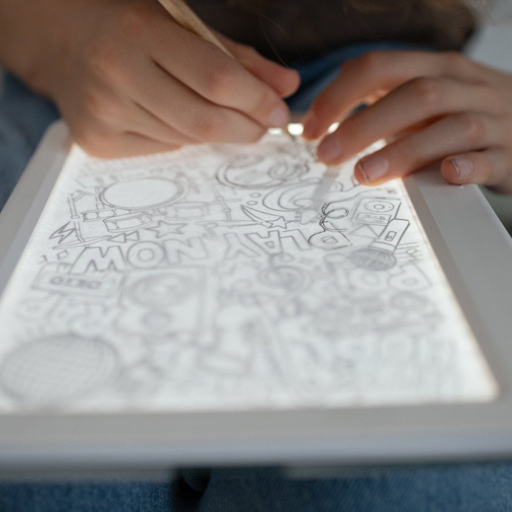 Close-up of hands tracing a music-themed drawing on the glowing KIDYDRAW light pad
