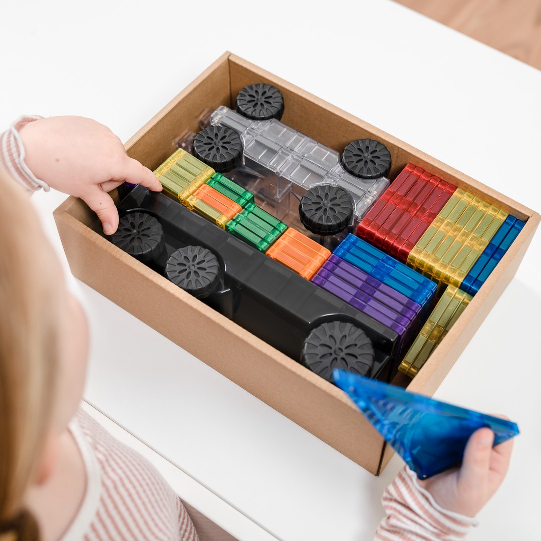 Child packing CONNETIX Rainbow Transport tiles and motion bases into the storage box