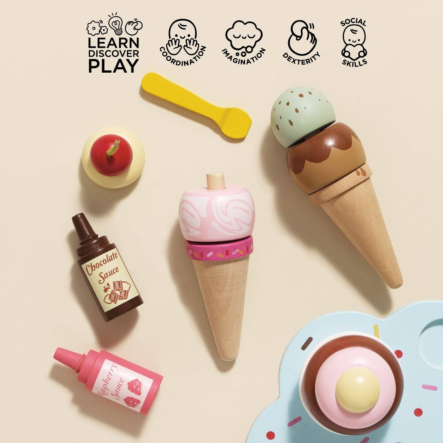 Toy ice cream set with cones, cherry, chocolate sauce, and strawberry syrup on a beige background.