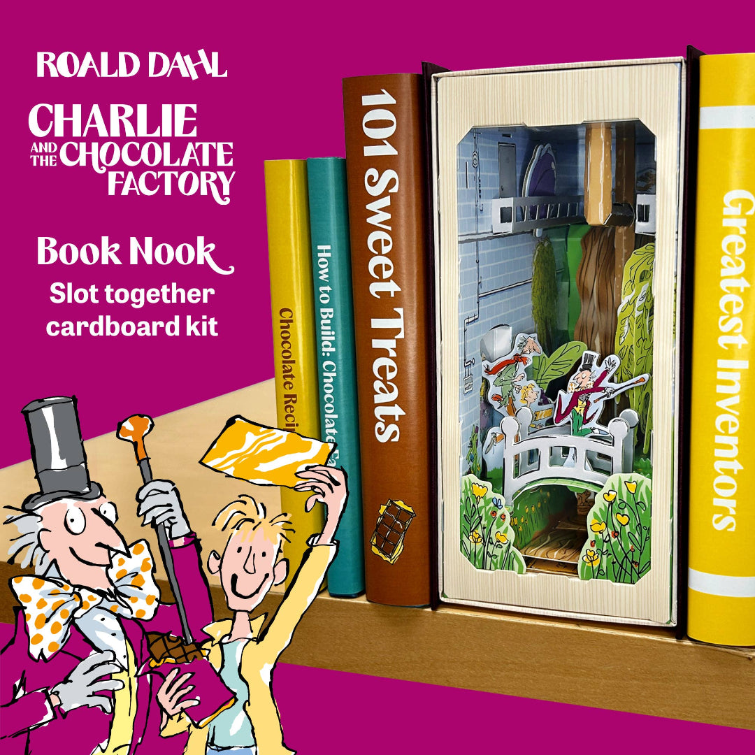 A colorful promotional graphic for a Roald Dahl 'Charlie and the Chocolate Factory' Book Nook slot together cardboard kit. The kit is shown assembled between decorative book spines on a wooden shelf, with cartoon illustrations of Charlie and the Mad Hatter on a bright magenta background.
