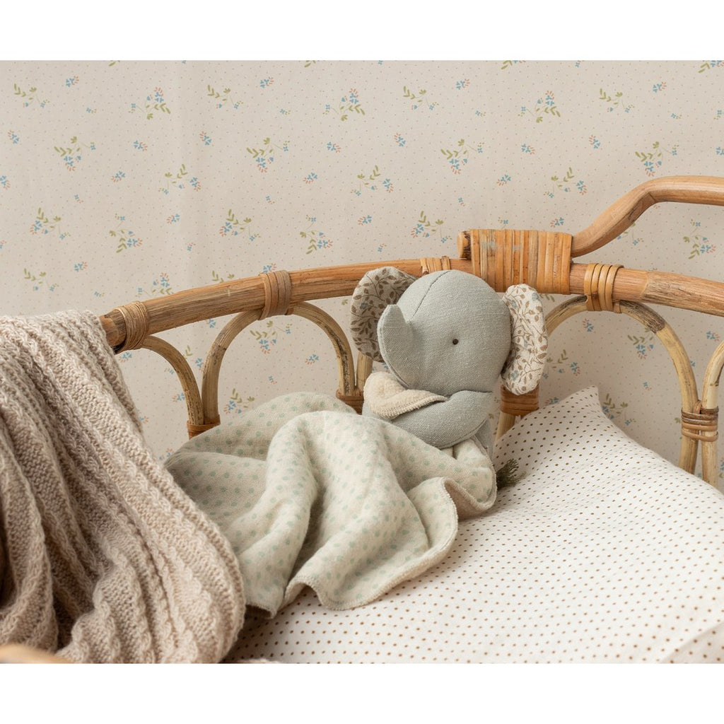 Maileg Lullaby Friends elephant tucked into a rattan doll's bed with a dotted blanket