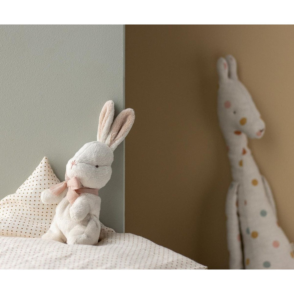 Maileg My First Bunny in powder sitting on a cot with a spotty giraffe plush