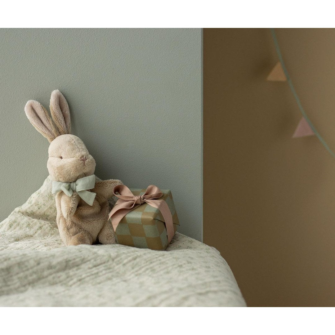 Maileg My First Bunny with mint bow on a bed beside a wrapped present