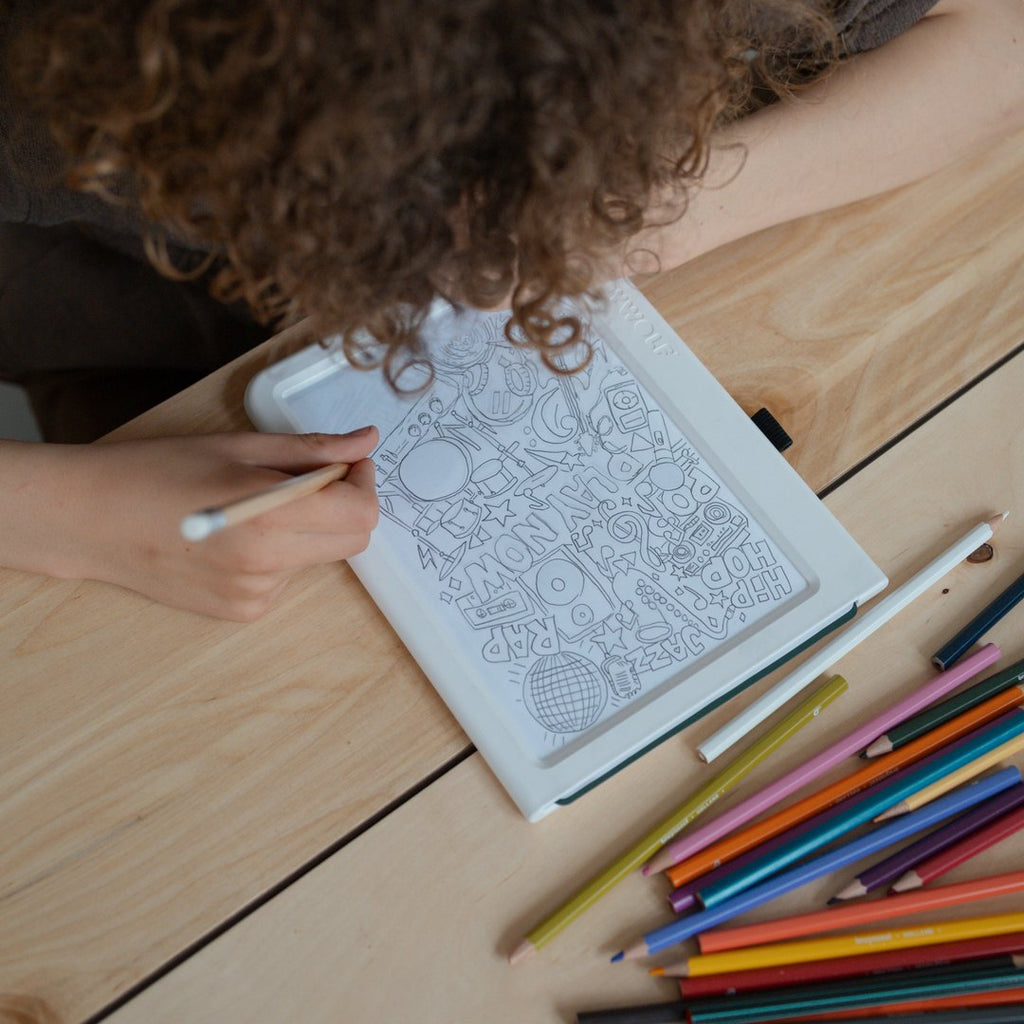 Child leaning over the KIDYDRAW light pad tracing a picture, coloured pencils on the table