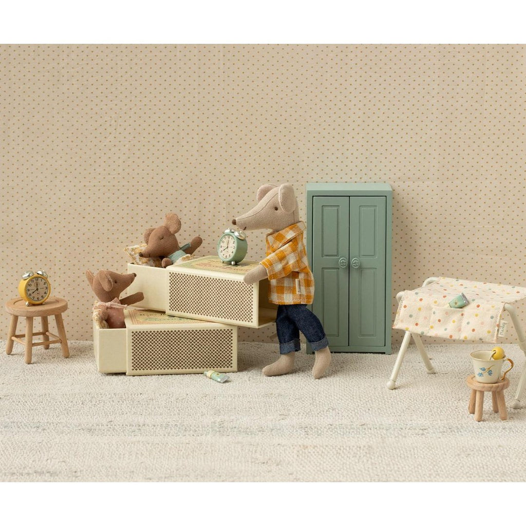 Maileg dad mouse putting baby mice to bed in stacked matchbox beds beside a mint wardrobe