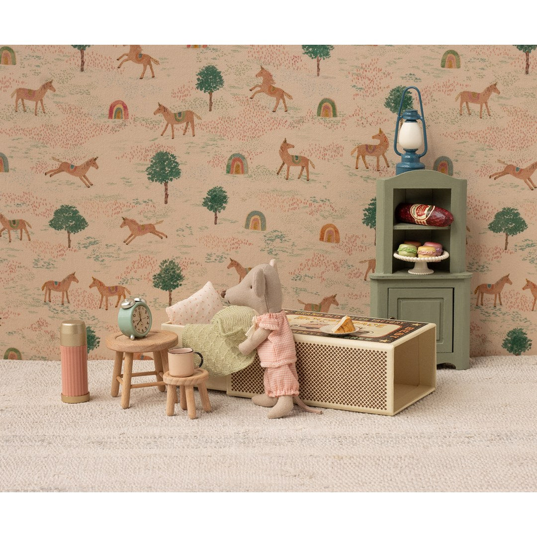 Maileg little sister mouse making her matchbox bed in front of horse wallpaper with a dresser and stools