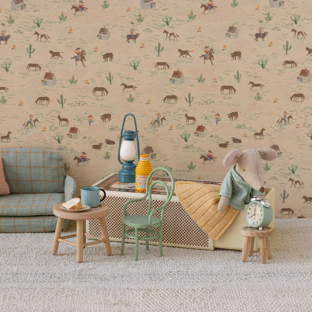 Maileg little brother mouse in pyjamas beside his matchbox bed with an alarm clock, lantern and mini sofa against cowboy wallpaper