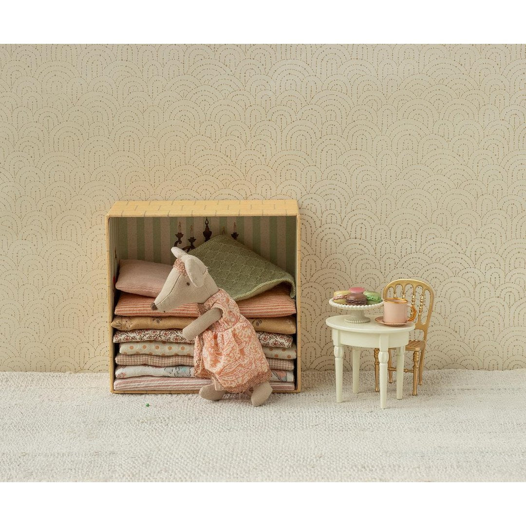 Maileg princess mouse climbing into her mattress bed beside a white table set for tea