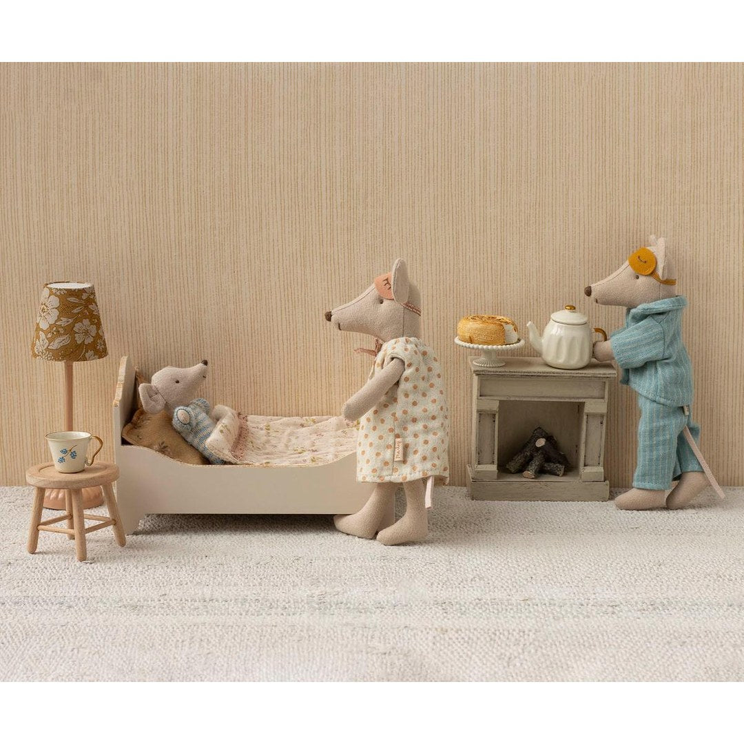 Maileg Mum and Dad mice tucking baby mice into bed by the fireplace with cake and a teapot
