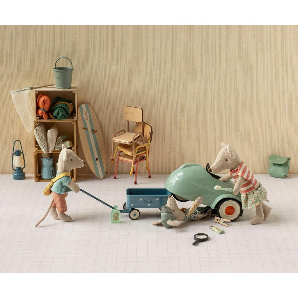 Maileg mice pulling a blue wagon and fixing a mint mouse car beside a surfboard, chairs and storage shelf