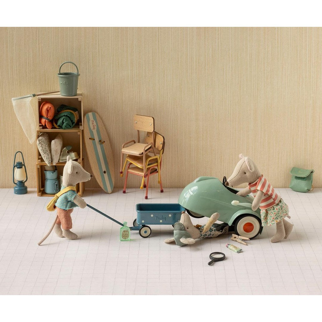 Maileg mice pulling a blue wagon and fixing a mint mouse car beside a surfboard, chairs and storage shelf