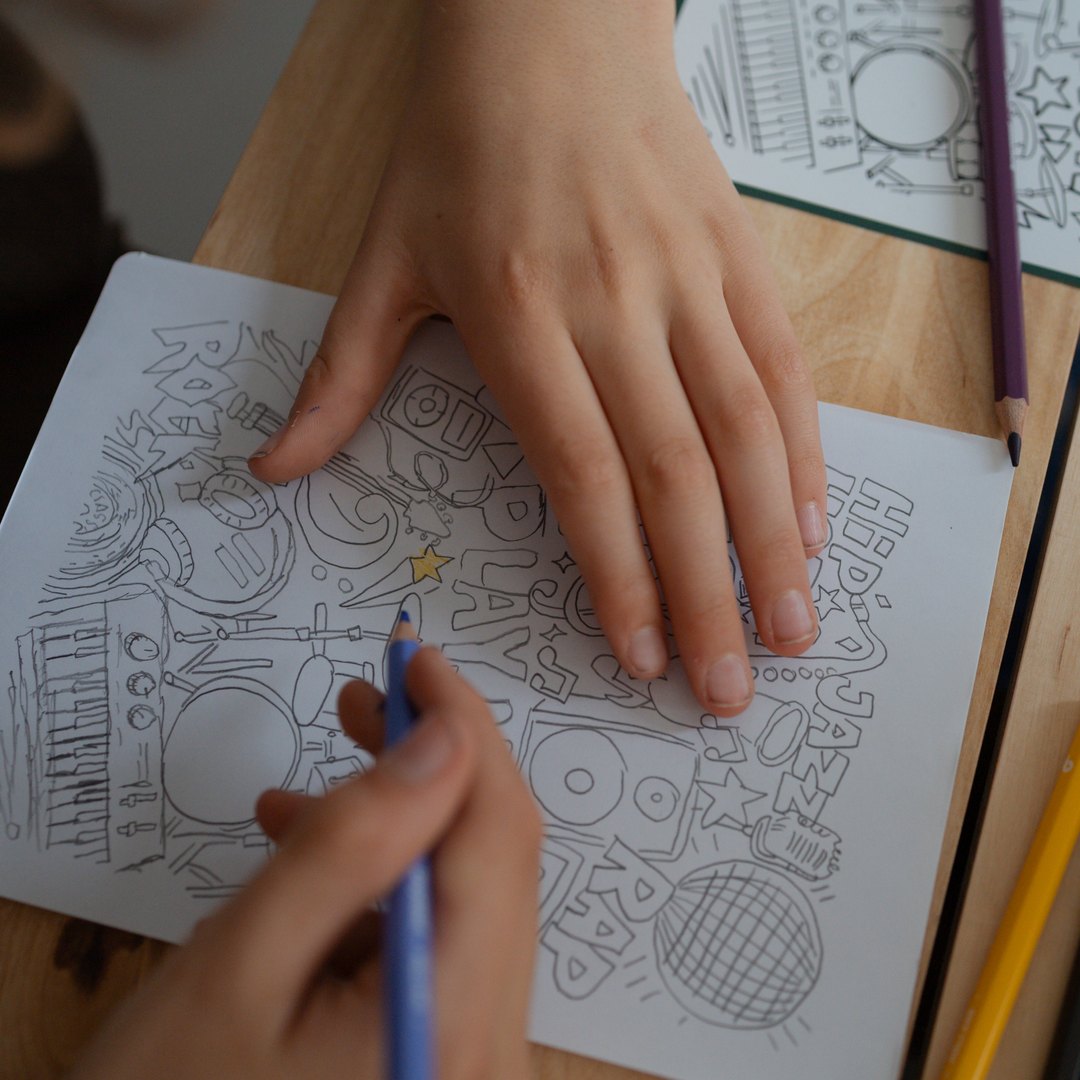 Child colouring in a traced Play Now music drawing with coloured pencils
