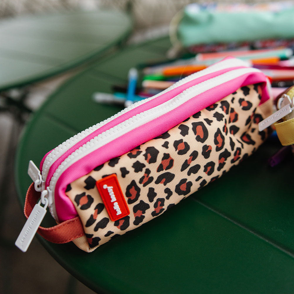 A leopard print pencil pouch with a bright pink zipper trim, resting on a green Chair