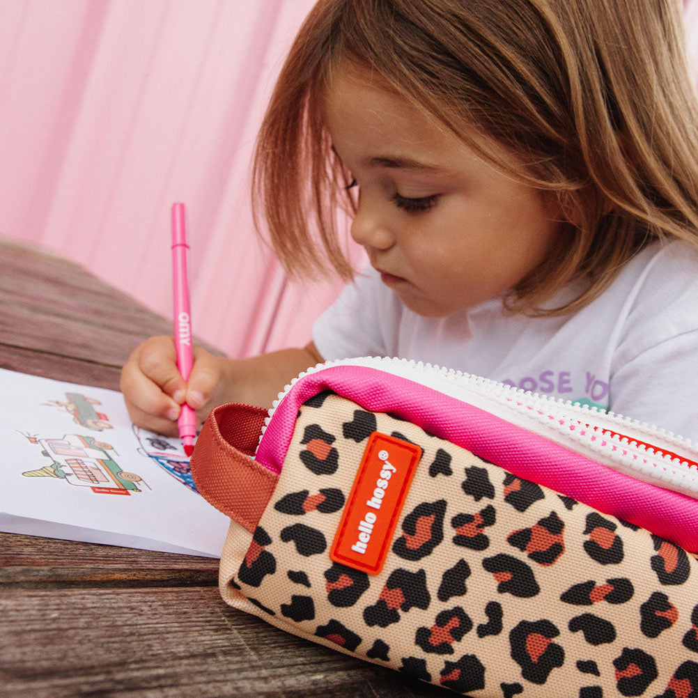 Child with a leopard print pencil case and pink pen on a wooden surface