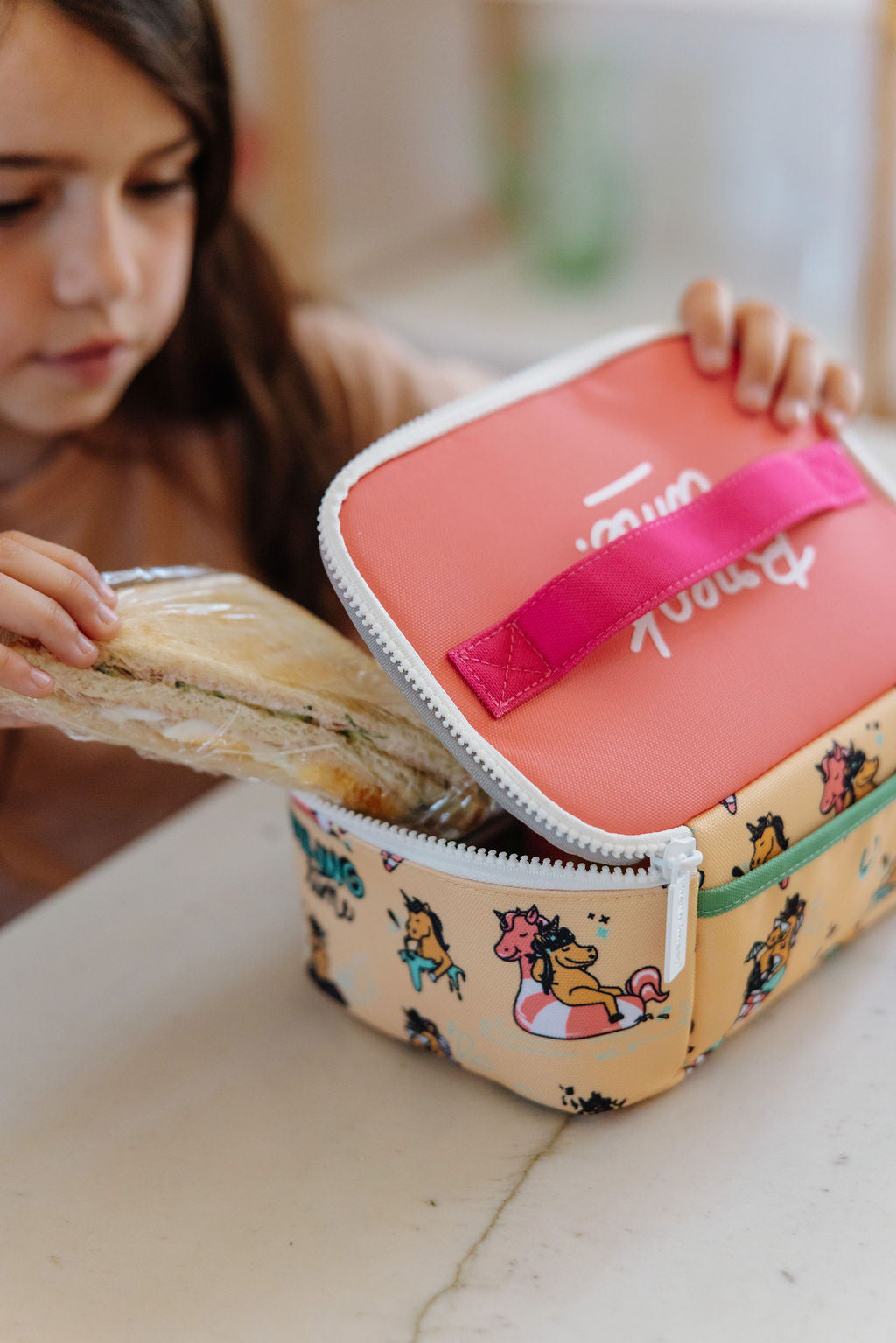 Child holding a colorful lunch bag with cartoon designs and a pink strap.