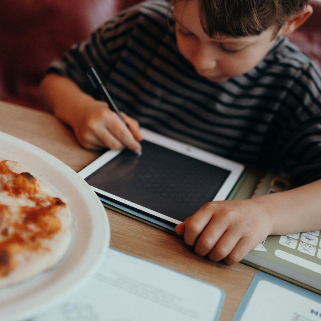 Child using a tablet with a plate of pizza on a table