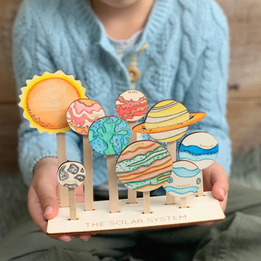 Child holding a model of the solar system with colorful planets on sticks.