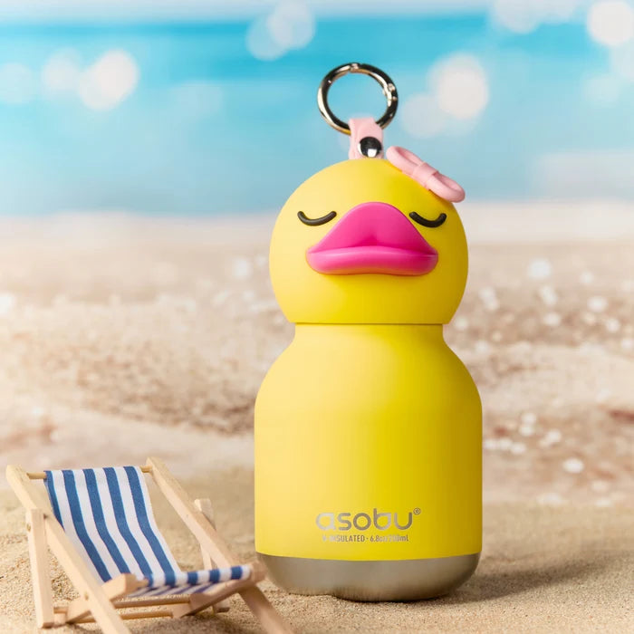 Yellow duck-shaped bottle with a pink lid on a beach with a small striped chair.
