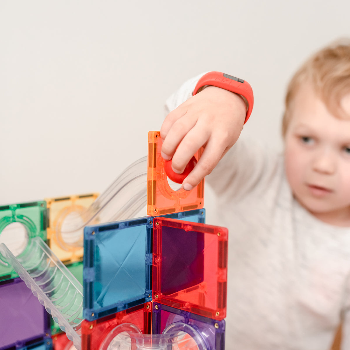 Young child building a rainbow CONNETIX magnetic tile structure for a ball run