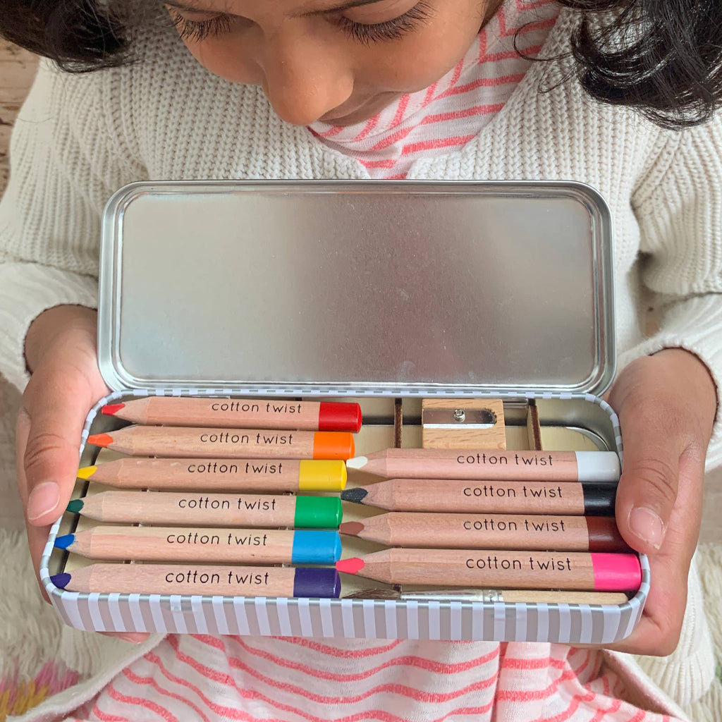 Child holding a set of colorful cotton twist pencils in a metal tin.