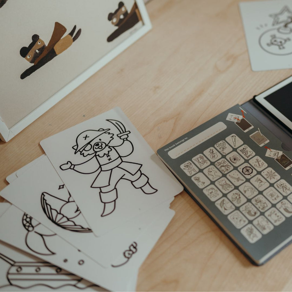 Pirate drawing cards spread on a wooden table next to the grey Oceans and Pirates card holder showing all the card designs