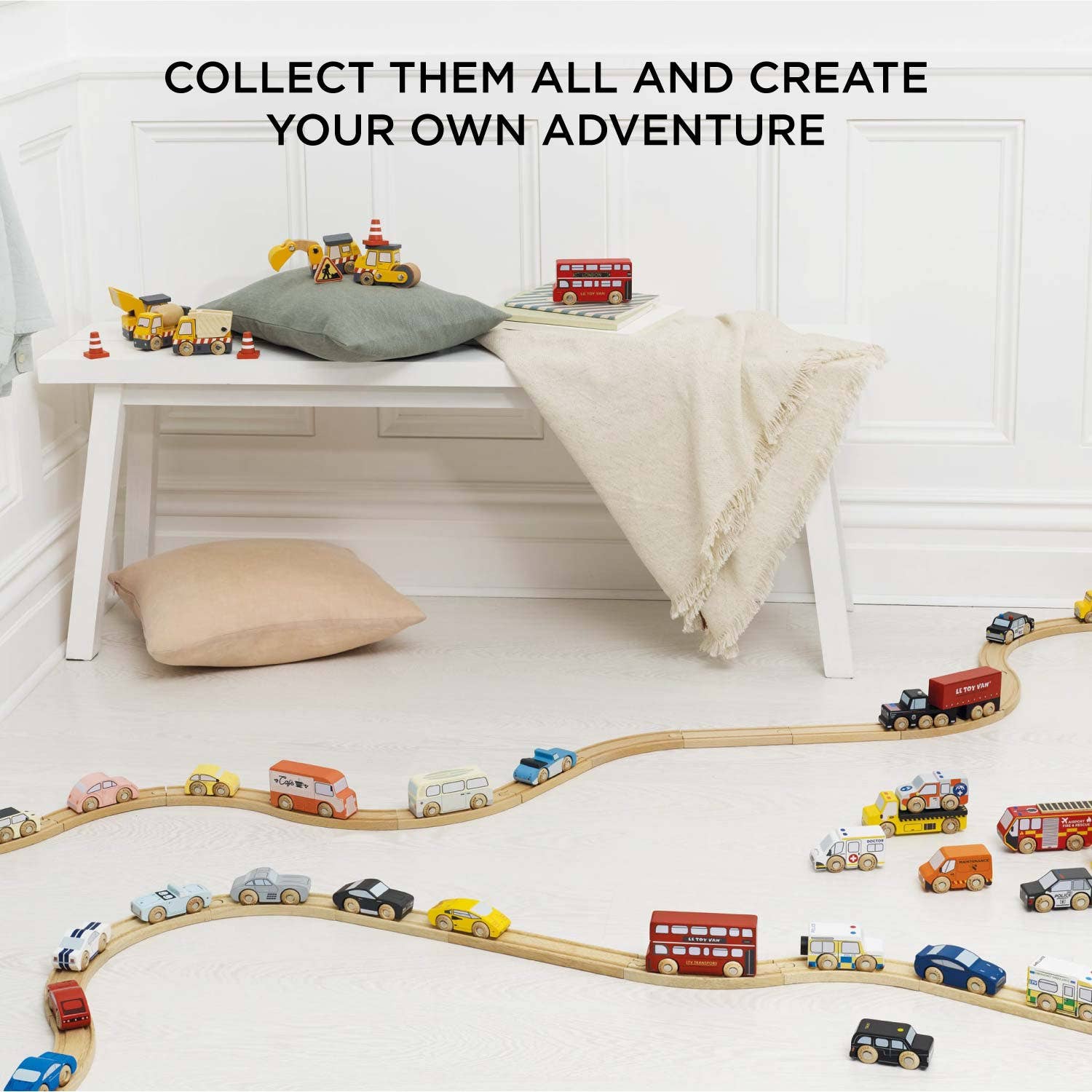 Wooden toy train set on a white floor with toys and a bench in the background.